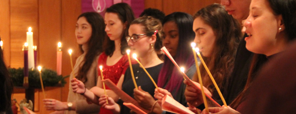 7 students standing in a row, holding candles during a prayer