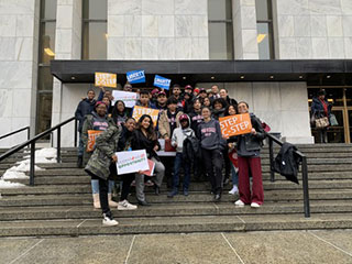 Students_standing_on_steps_smiling_and_holding_signs