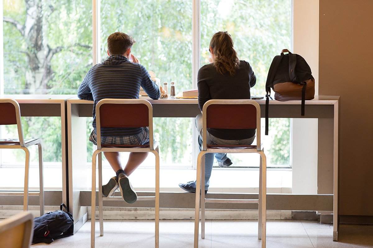 Two students sitting on stools in a dining hall