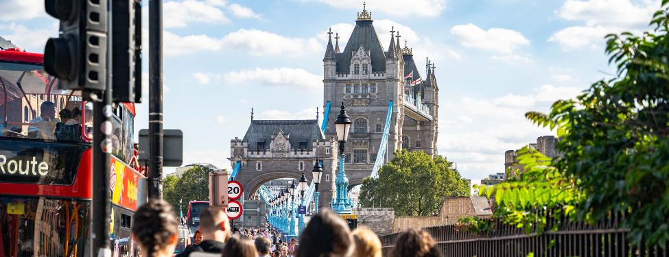 a photo of students walking toward London's Tower Bridge. A red, double-decker bus is on the left hand side.