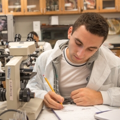 Male student in lab coat writing notes - LG