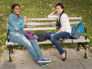 Two female students sitting next to each other on a bench at the Rose Hill campus