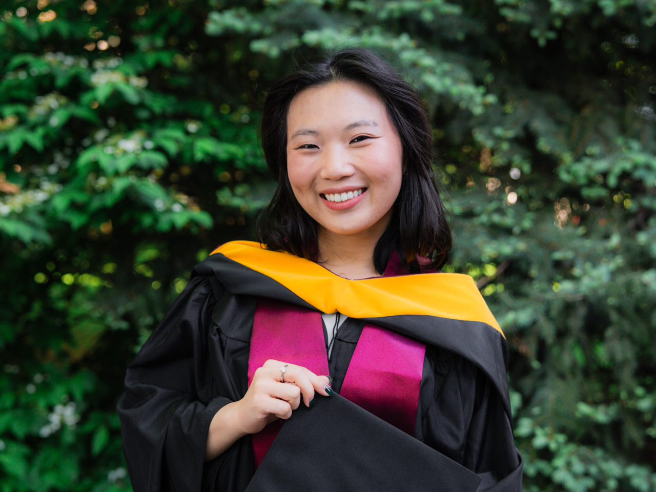 Tuchau Ly posing in front of shrub at 2026 Commencement at Rose Hill