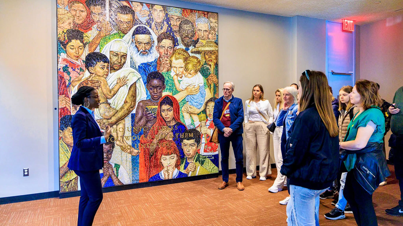 A woman standing in front of a painting talking to a large group of people