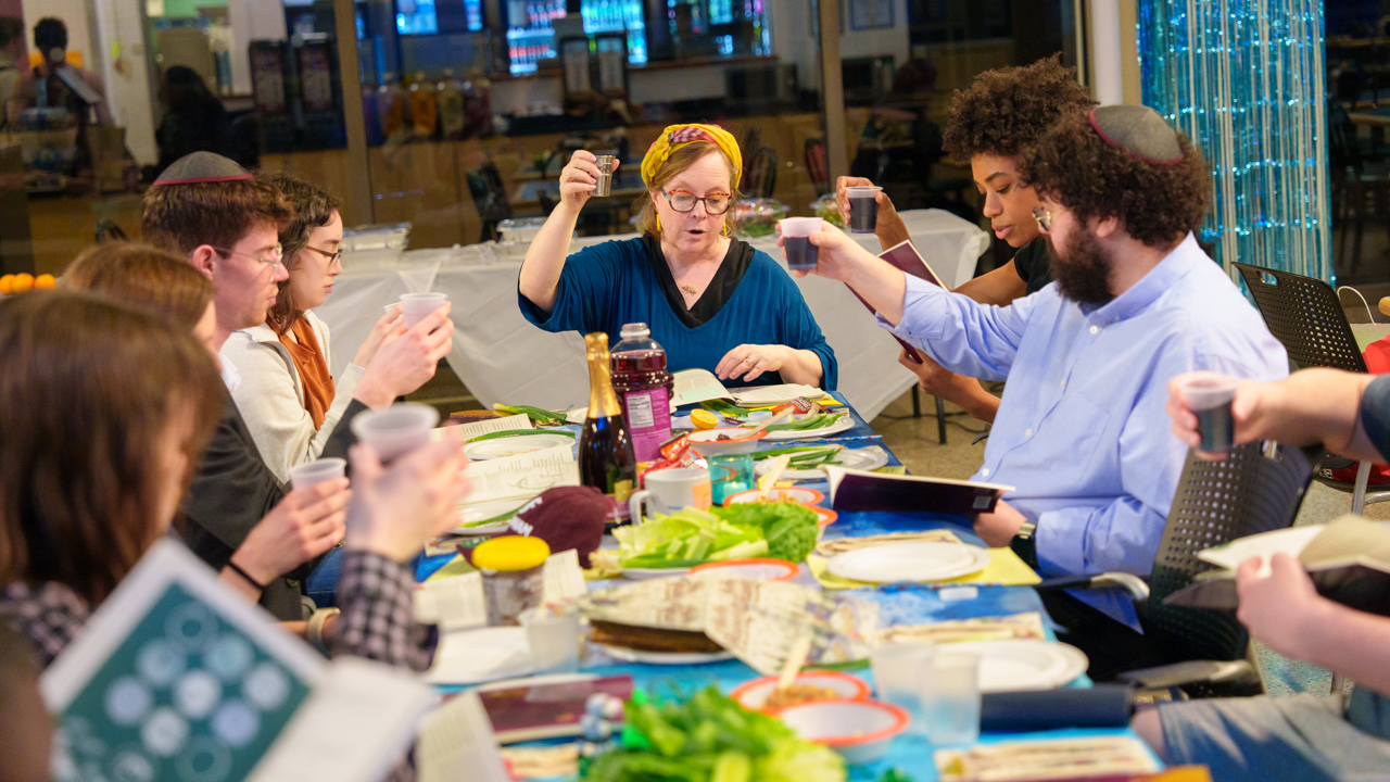 People sitting at a table laden with food and drink raise their drink glasses.