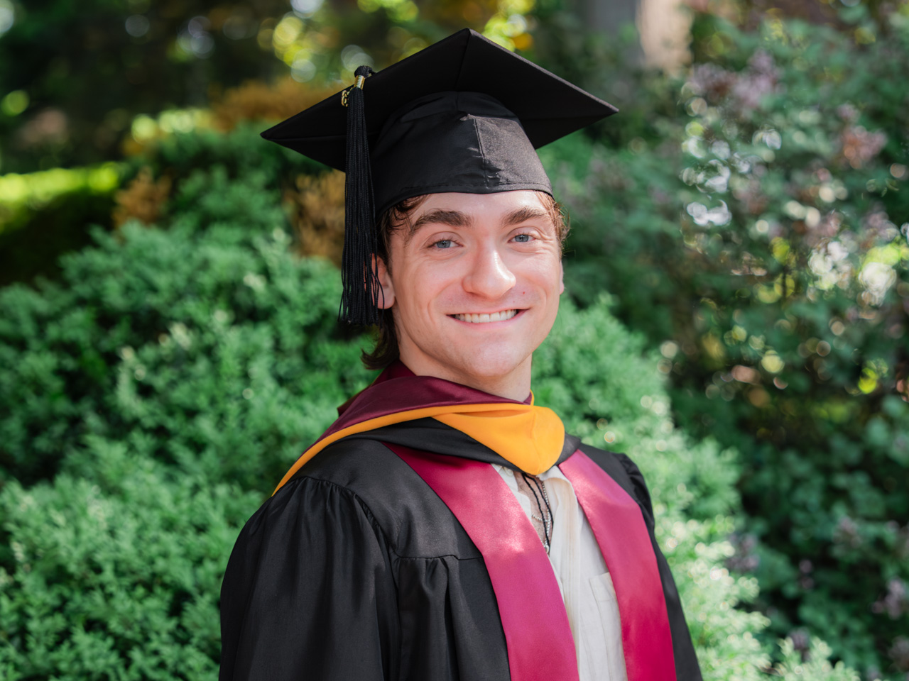 Bryce Vitale standing in front of a shrub at Fordham's Commencement at Rose Hill