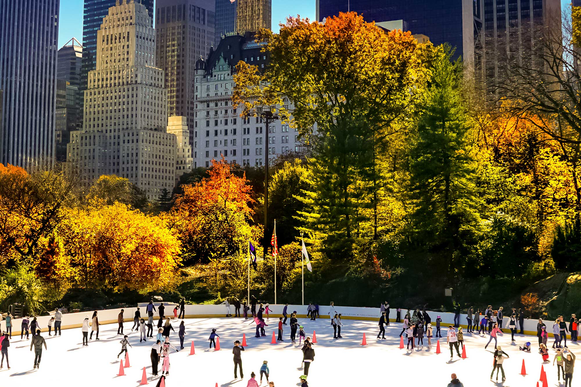 People ice skate on Wollman Rink in Central Park on a bright sunny day.