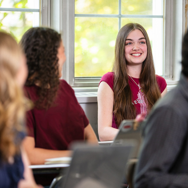 Student smiling in back row of a classroom at Rose Hill