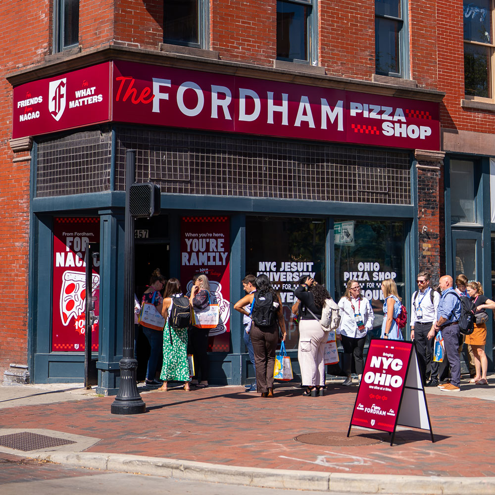 An exterior shot of the Fordham Pizza Shop at the NACAC Conference in Columbus Ohio with a long line on the sidewalk