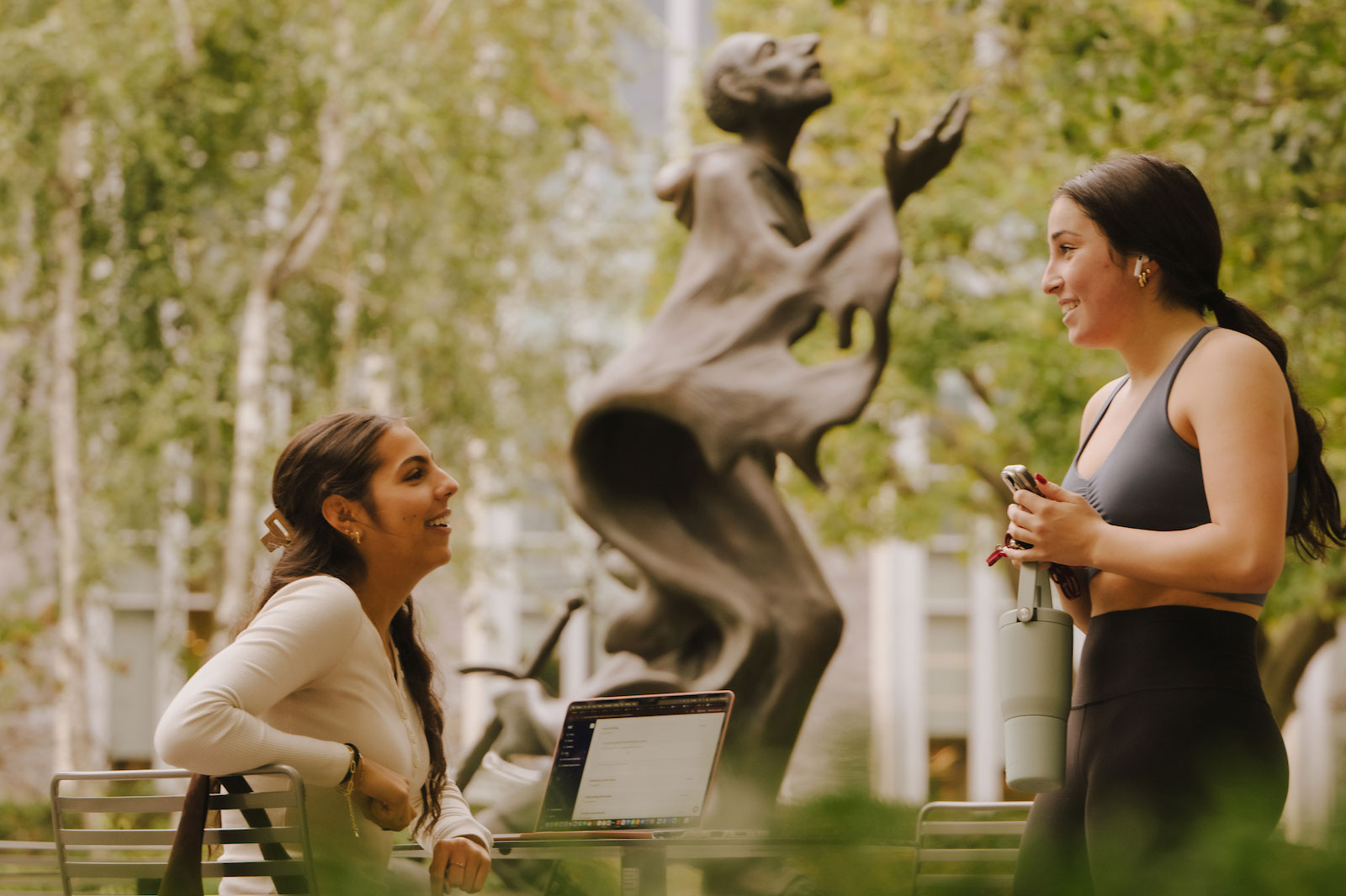 Two students catch up between classes on campus in front of the Saint Ignatius statue