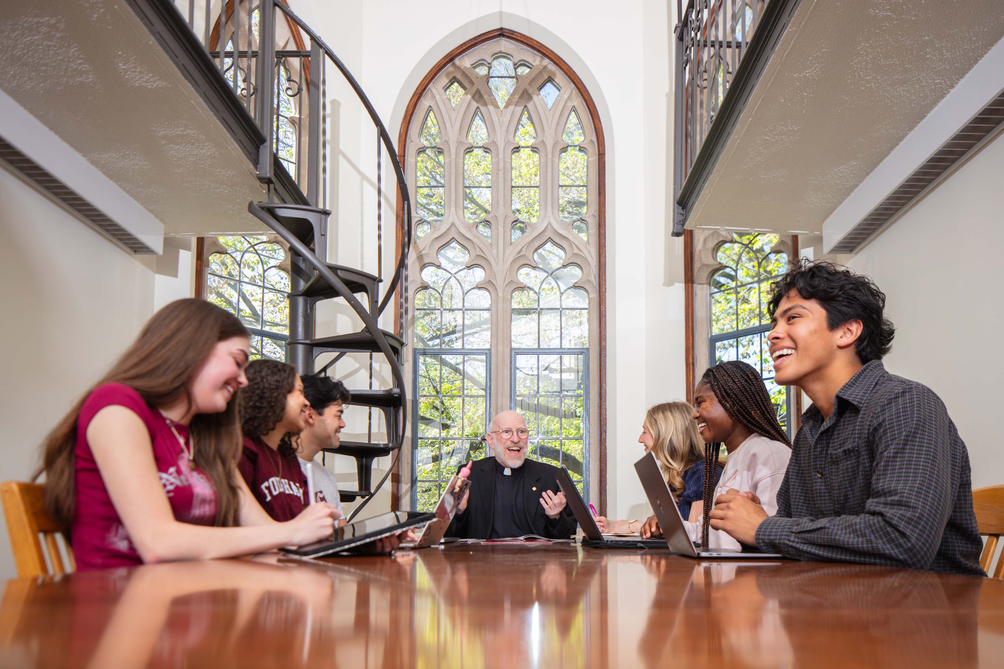 six students at table smiling with priest