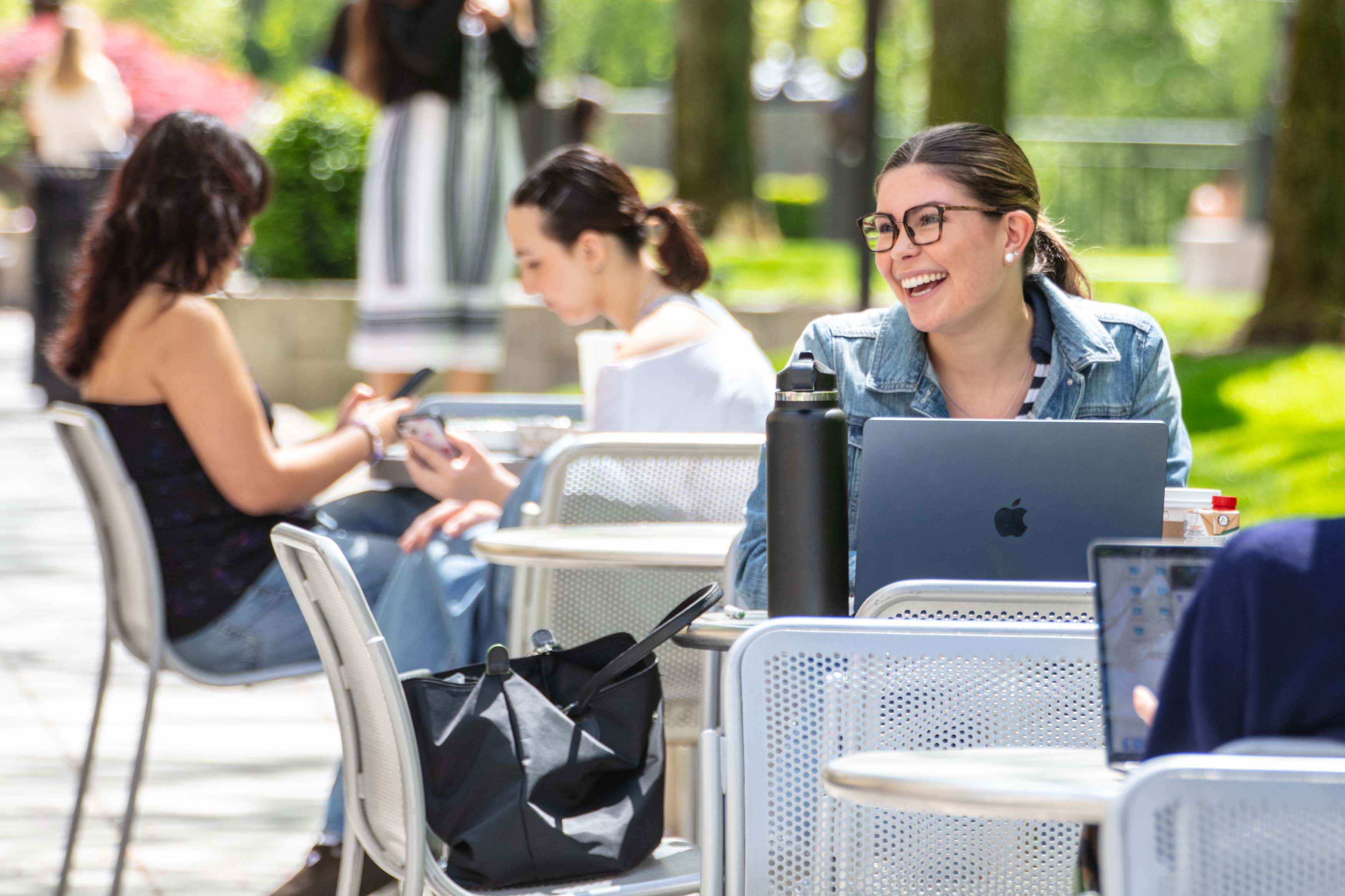 student smiling sitting outside on campus with laptop