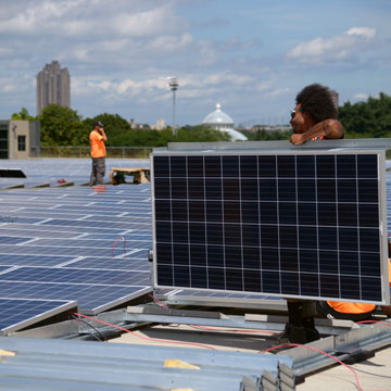 Workers installing solar panels on top of a building on the Rose Hill campus