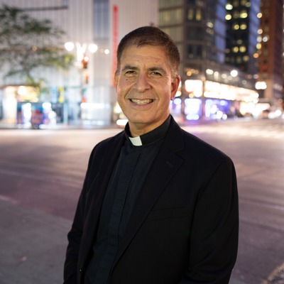 Priest in collar standing in Columbus Circle with streelights