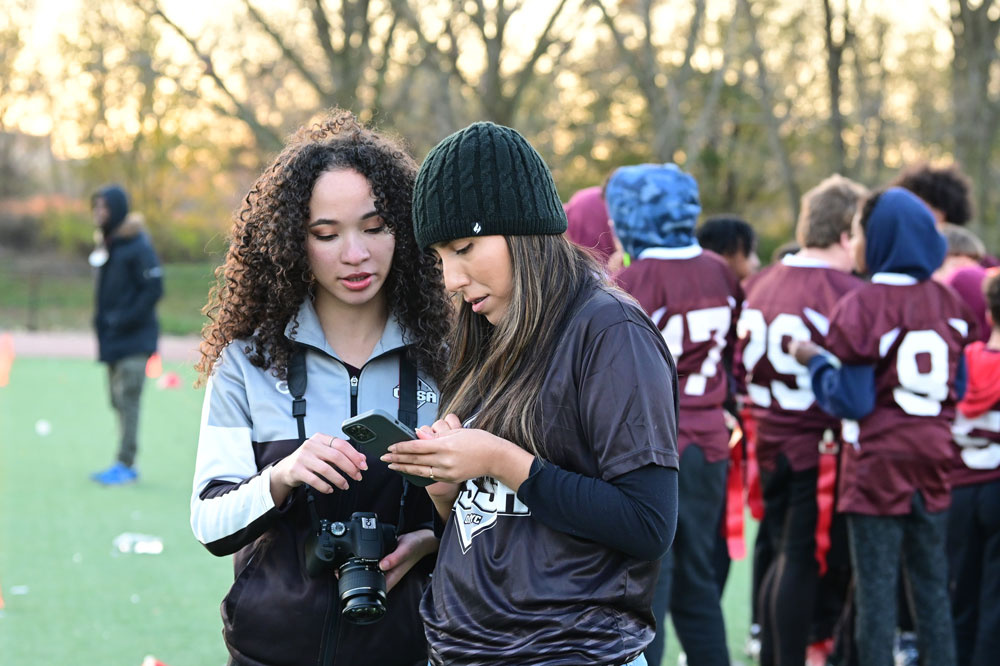 Two student interns look at photos taken at a youth soccer game for social media