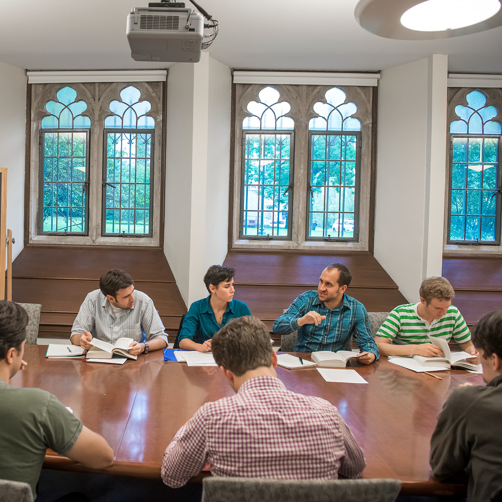 Group of Students in a Meeting Hall with Windows Having a Discussion while Reviewing Notes and Readings.
