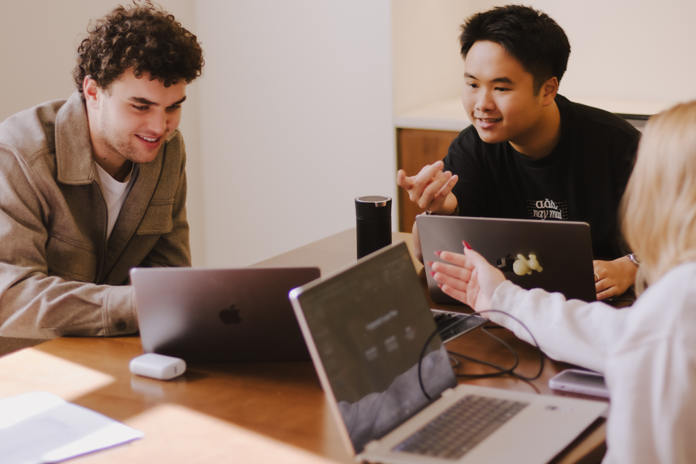 Three students on their laptops work together on a class project at a table