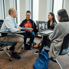 A professor sits down with students in a classroom during small group work