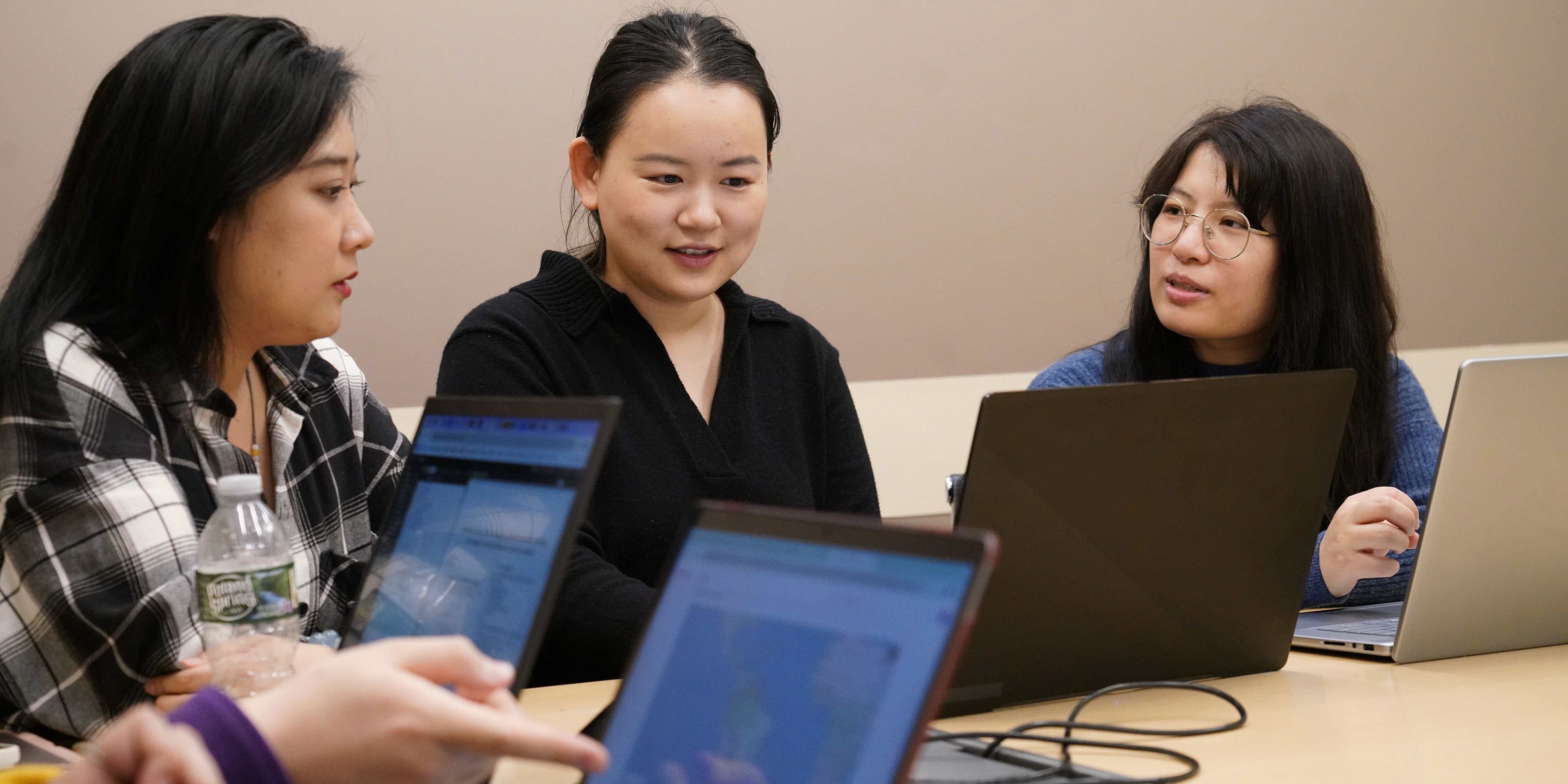 Three students sitting with laptops in classroom