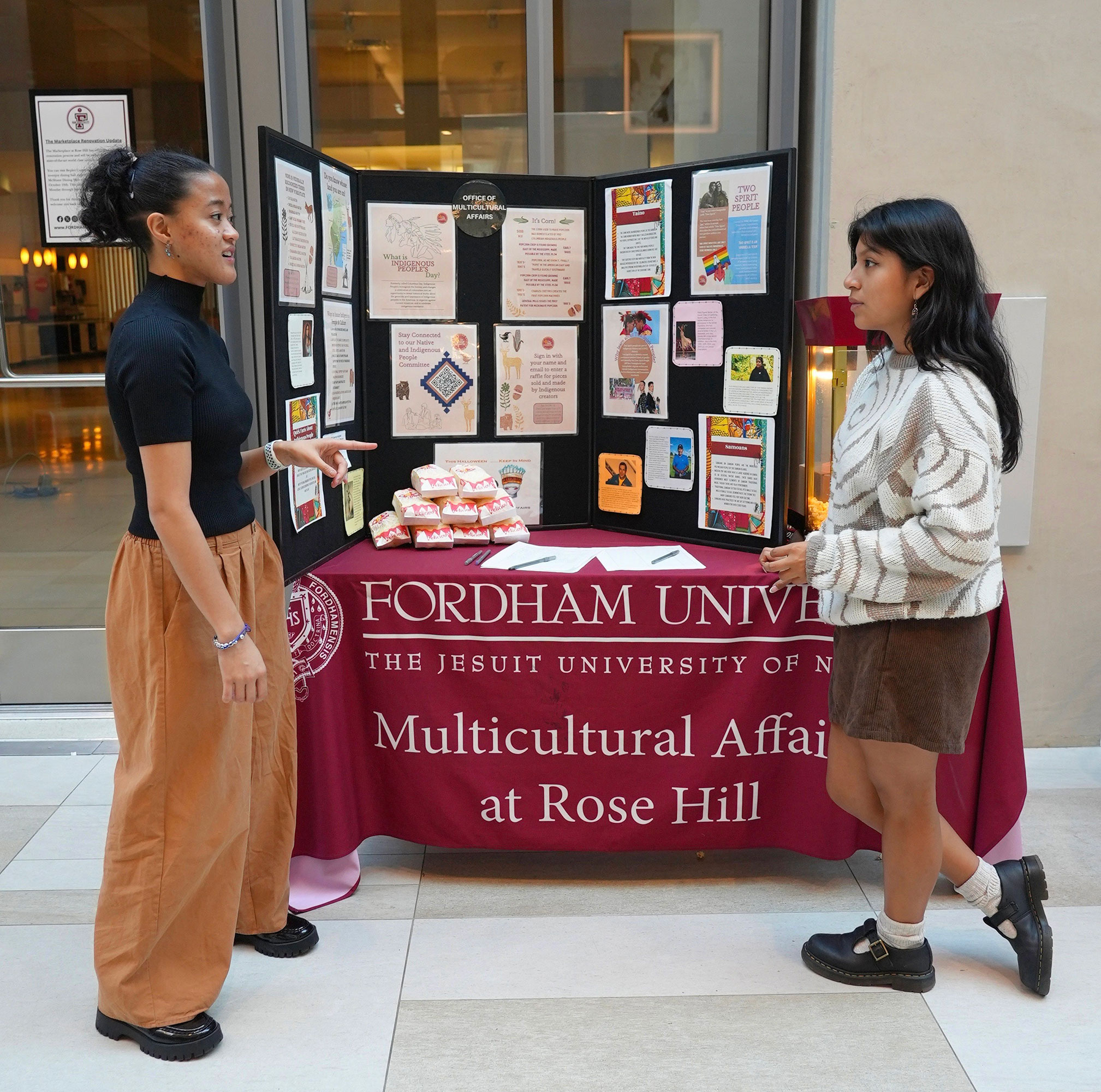 Two students stand in front of a table for the Office of Multicultural Affairs on Indigenous People's Day