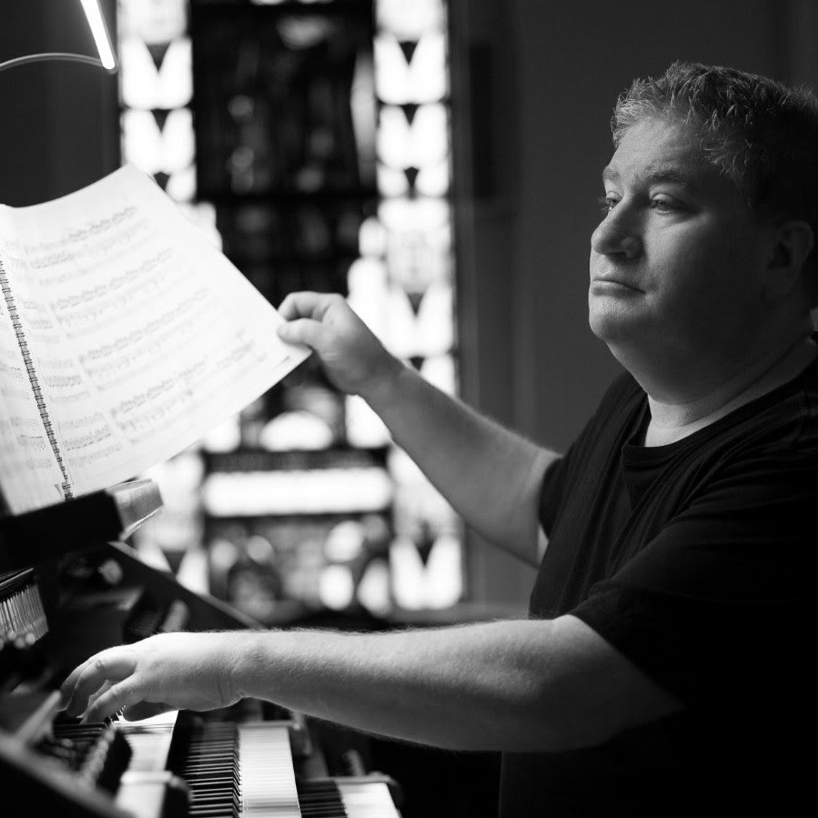 Father Steven Schloesser, St. Ignatius of Loyola Chair, reading and playing sheet music on a piano.