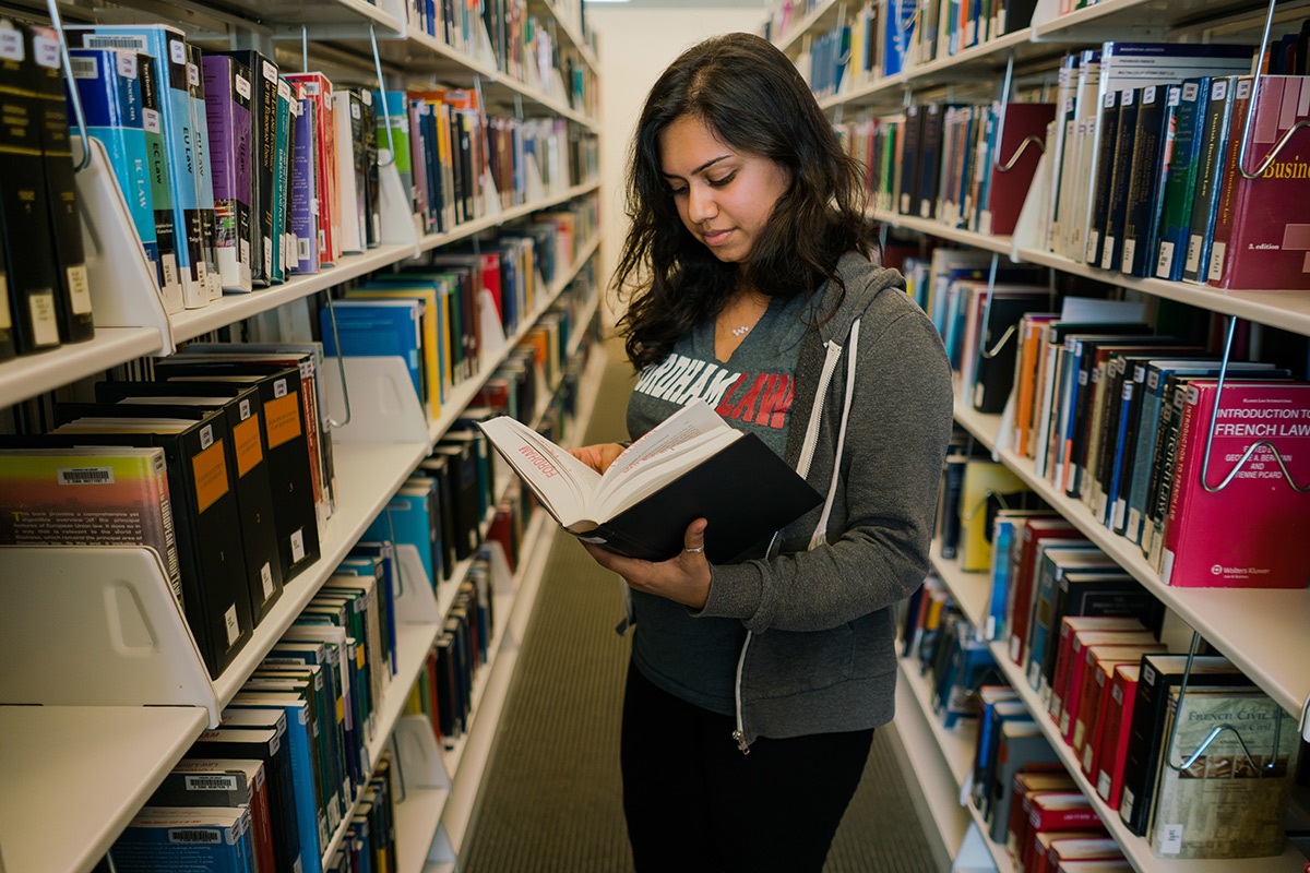 Female law student skimming a book in the the law library stacks