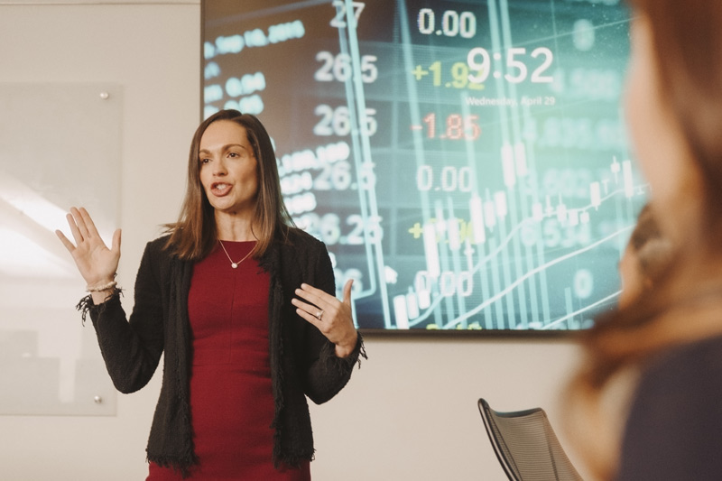Gabelli professor gives a lecture with a stock ticker in the background