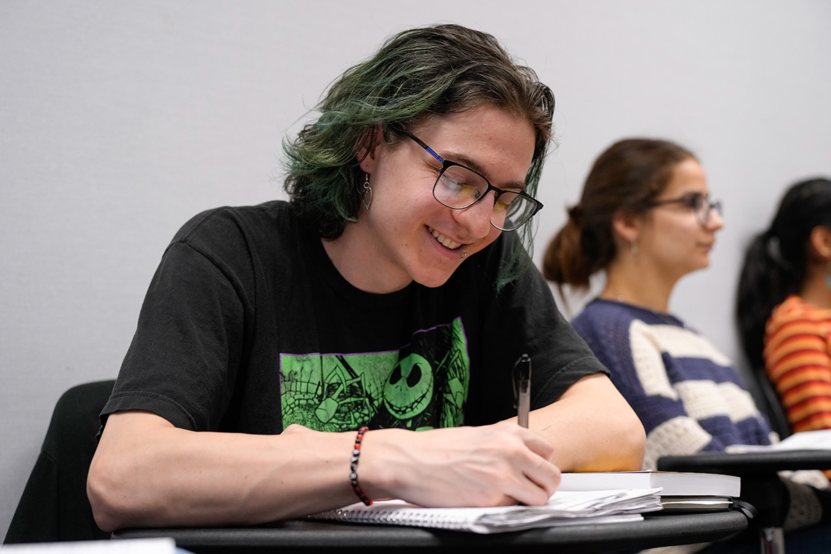 Male student writing in a notebook with a smile on his face