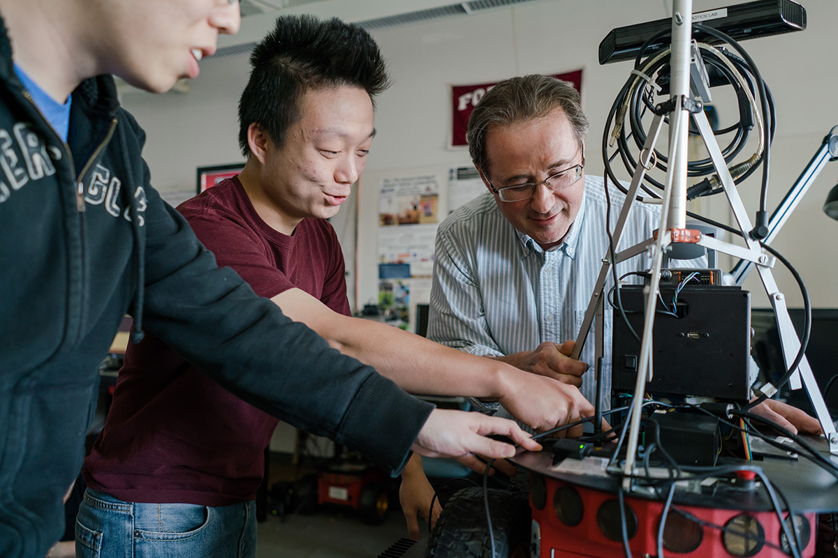 Two male students working with a professor on a robotics project