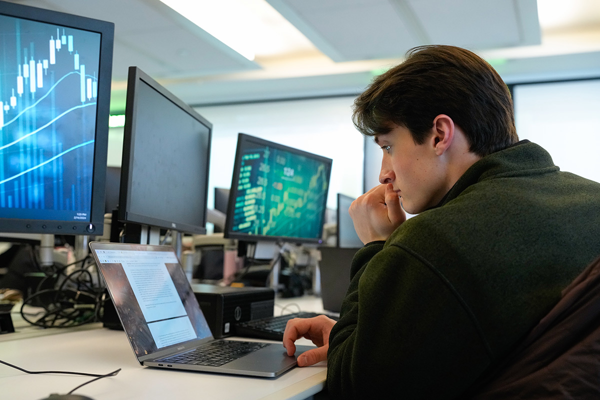 Male student working at a laptop along with three flat panel monitors