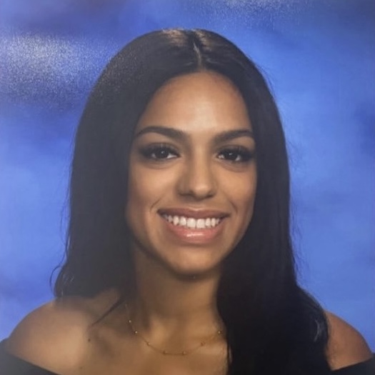 student in black dress and blue background smiling