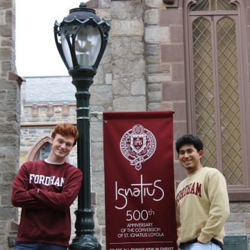 Two students standing next to a pole with a banner of the Ignatius 500 anniversary.
