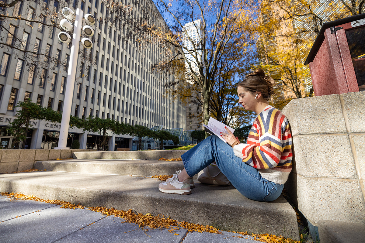 Student sitting under a tree at Lincoln Center in the fall
