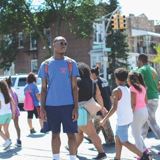 A worker from the NYC summer employment youth program, escorting children across a city street