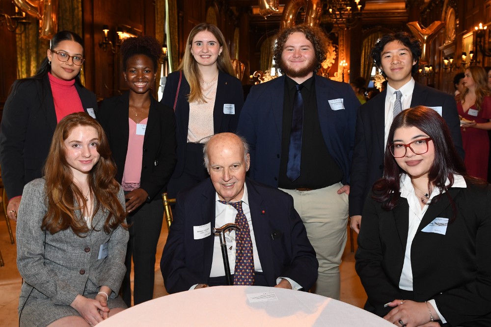 Two students sitting with a male donor with five additional standing behind them at the Scholarship Donors and Recipients Reception 2023