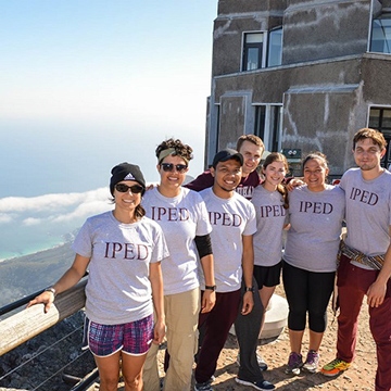 Students in IPED shirts posing for a group photo with ocean in background