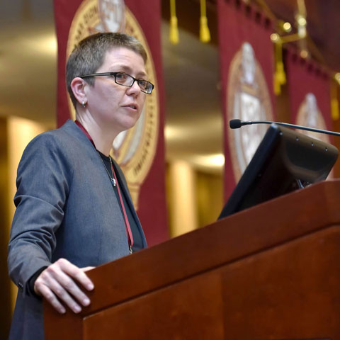 Professor Magda Teter lectures from podium with Fordham banners behind her