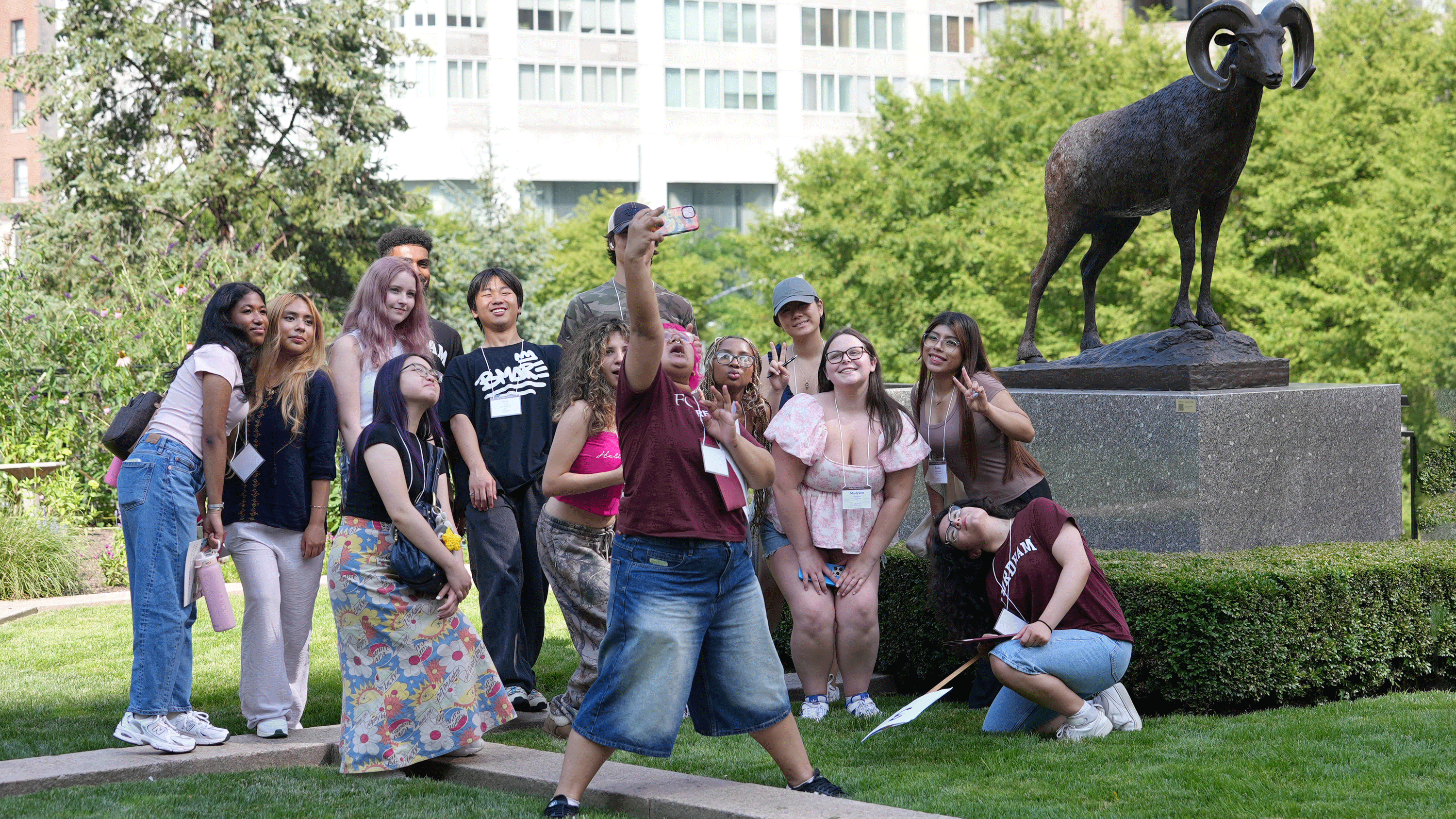 Students participating in summer orientation pose for a selfie outside in front of the Ram statue on the Lincoln Center campus