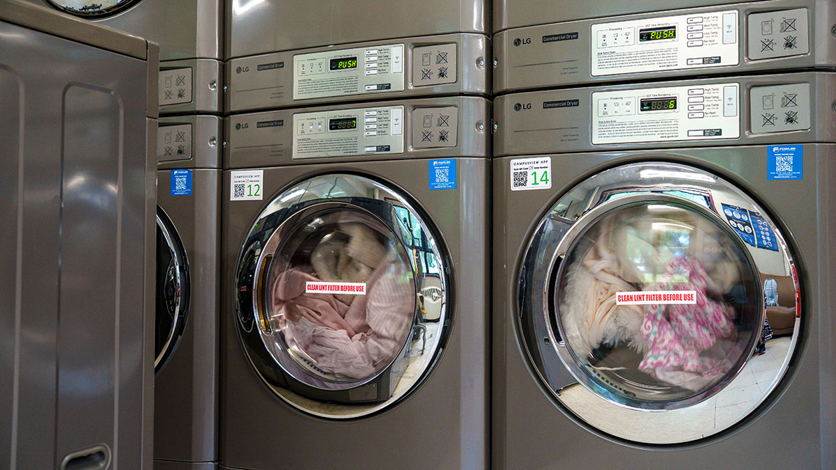 A row of industrial laundry machines with clothes inside, each displaying a digital timer.