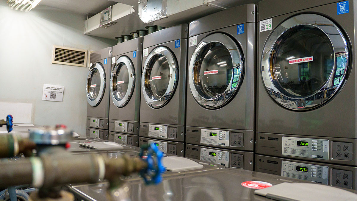A row of industrial washing machines in a laundromat, with digital displays and control panels.