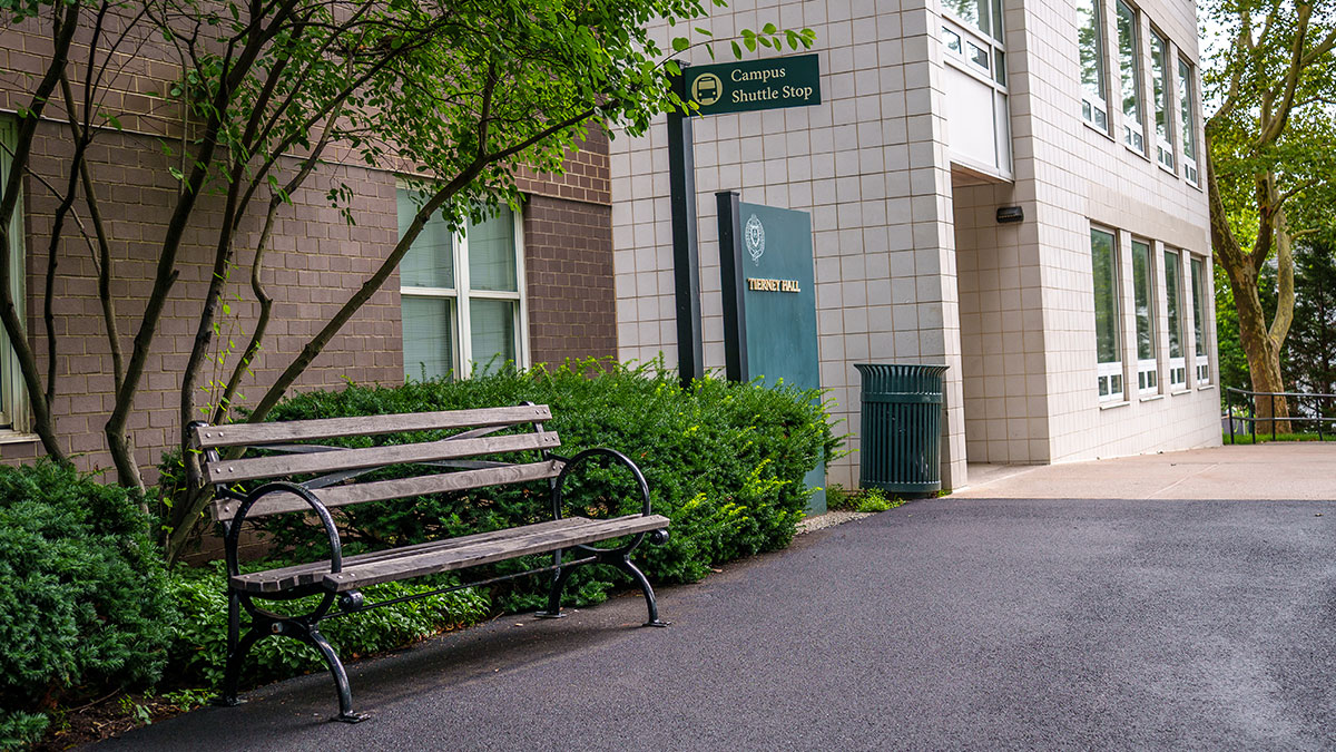 Bench and greenspace outside of Tierney Hall with a campus shuttle sign in the background