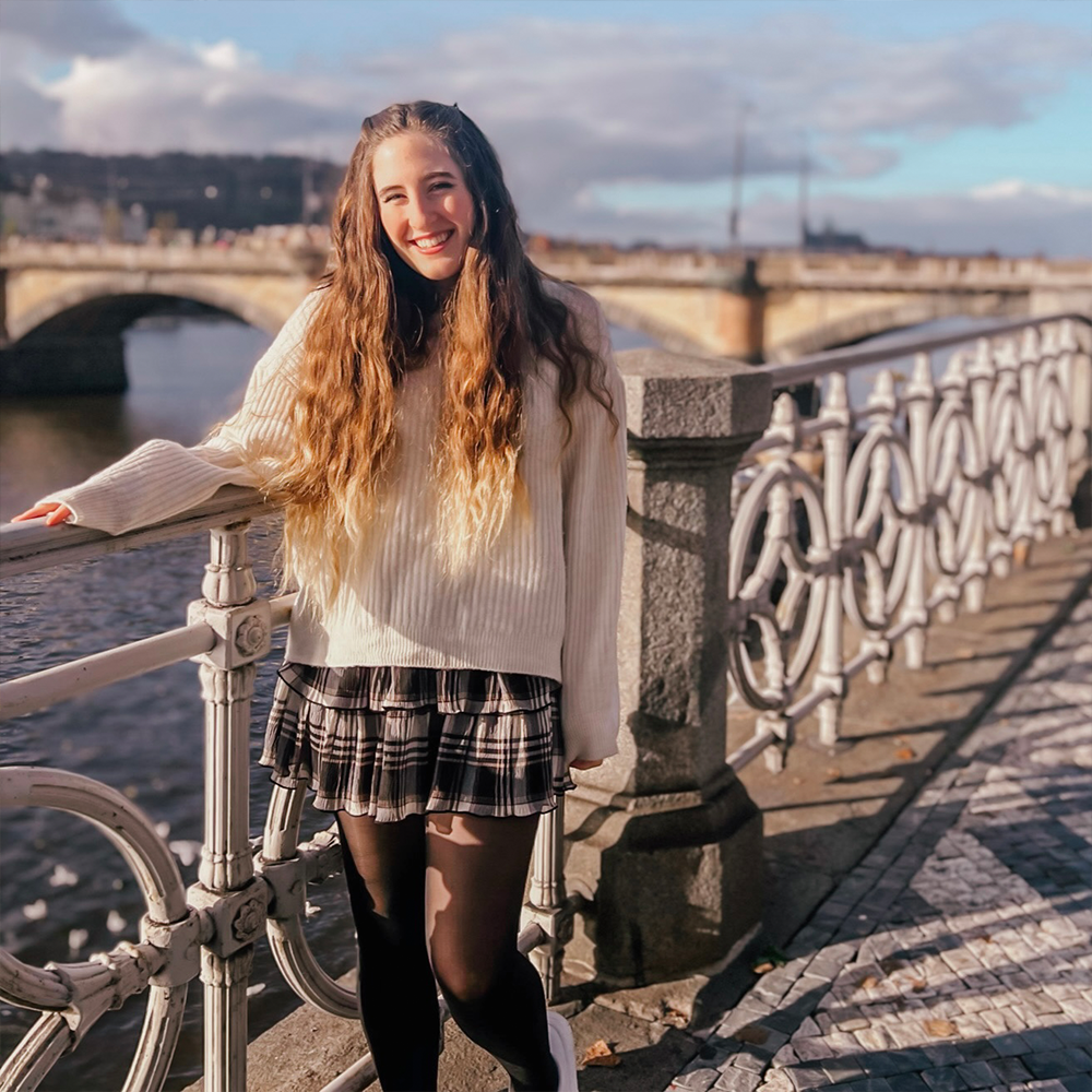 Student stands in front of bridge and river
