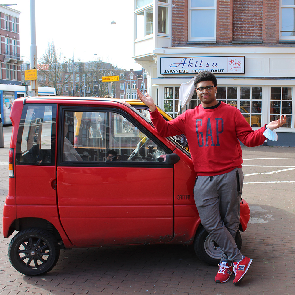 Student stands in front of a small red car