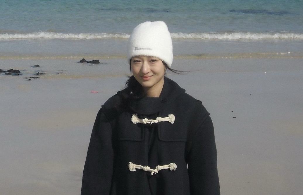 Student standing in a coat at the beach