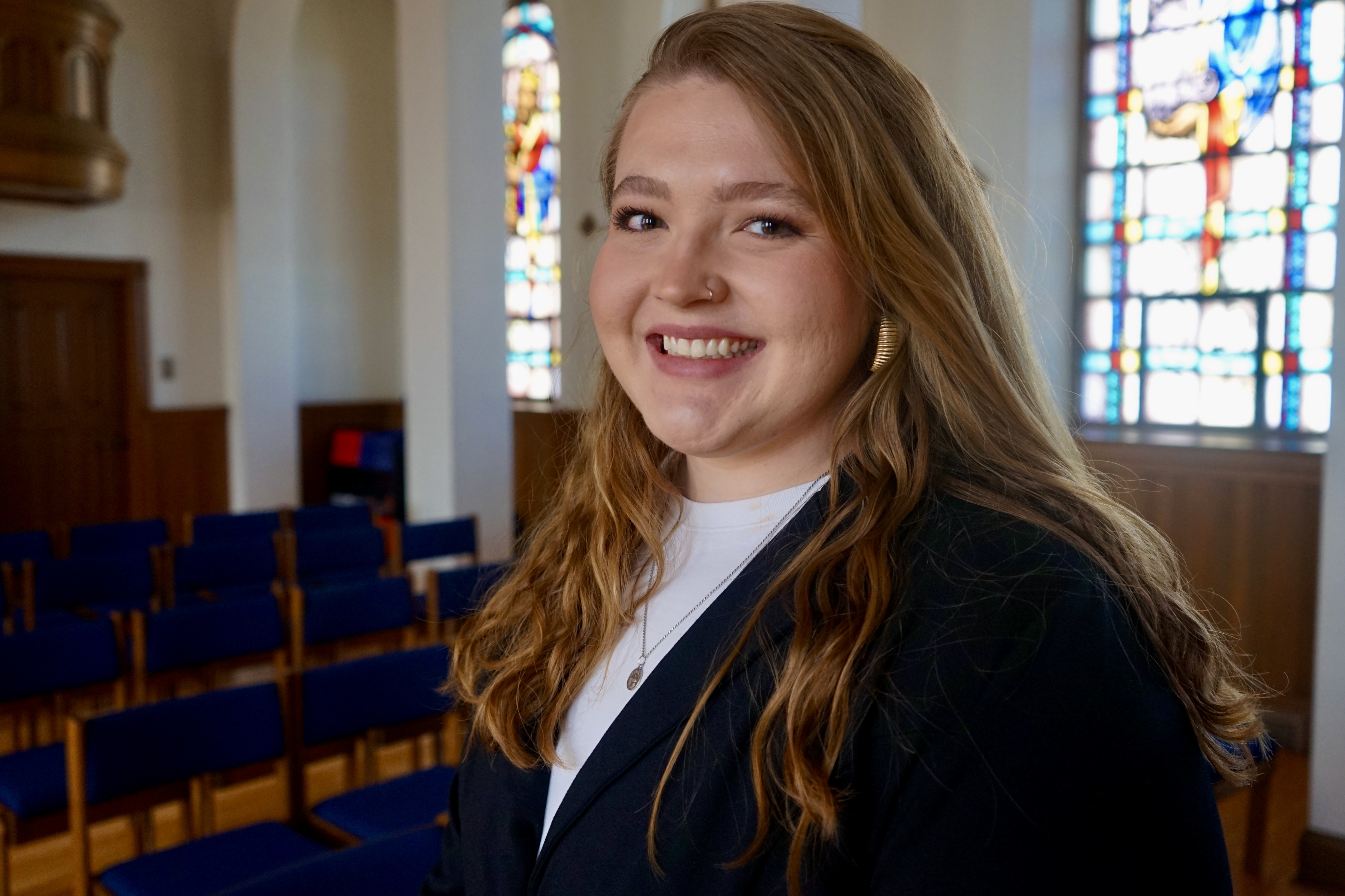 A headshot of Graceann Beckett, in a church with long red hair wearing a white shit with a black cardigan and smiling at the camera