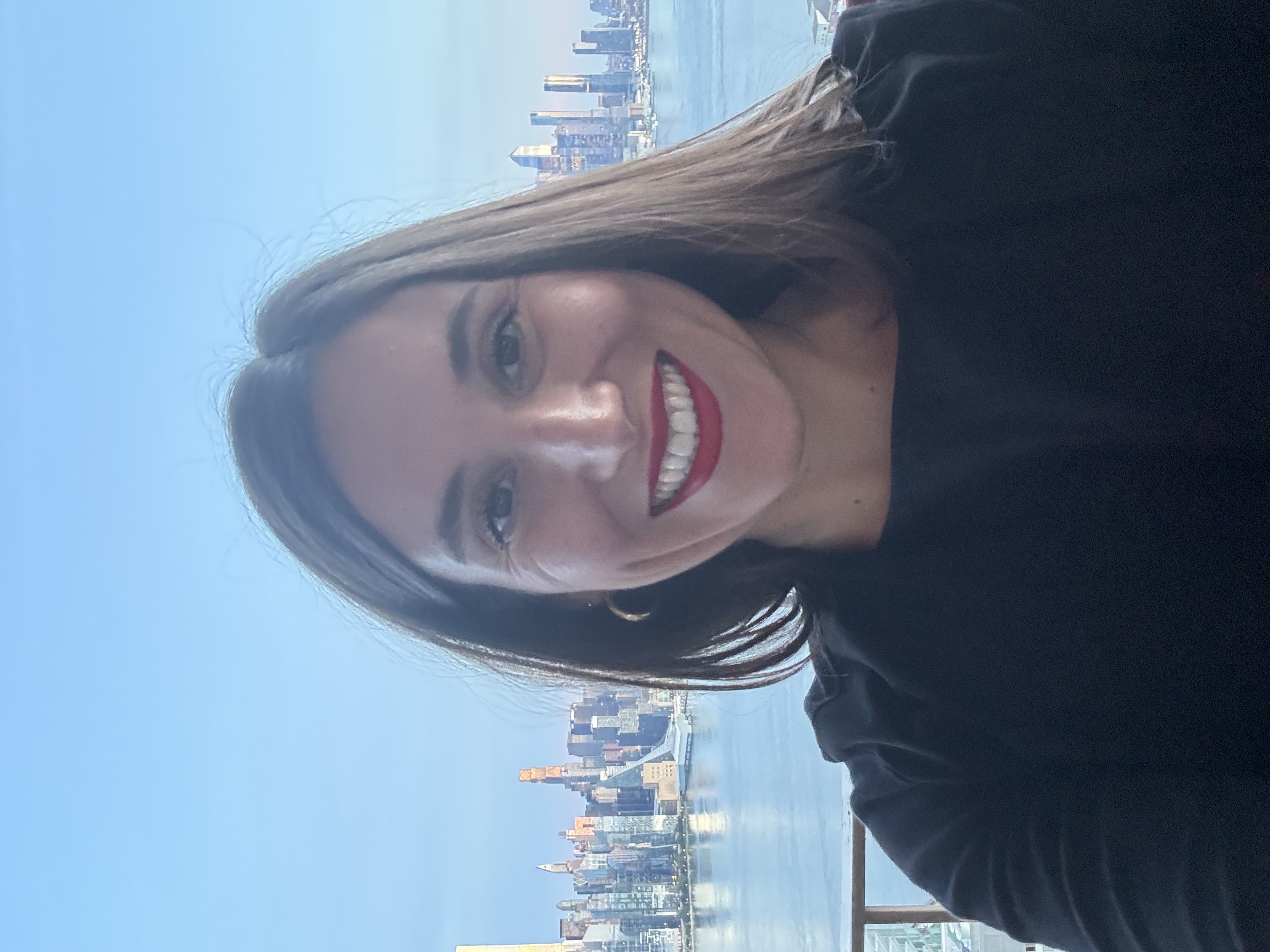 A headshot of Dina Zingaro, with shoulder length brunette hair and wearing a black shirt while smiling at the camera,