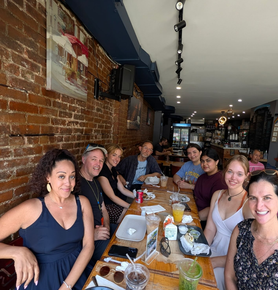 Several staff, faculty, and students sitting around a table, having lunch and smiling at the camera