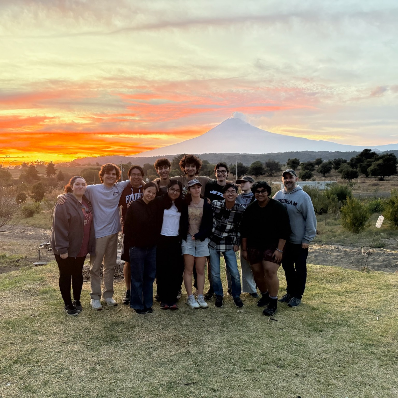 A group of people with a sunset and mountains behind them