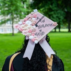 graduate wearing pink graduation cap with flowers on it. the text on the cap reads,