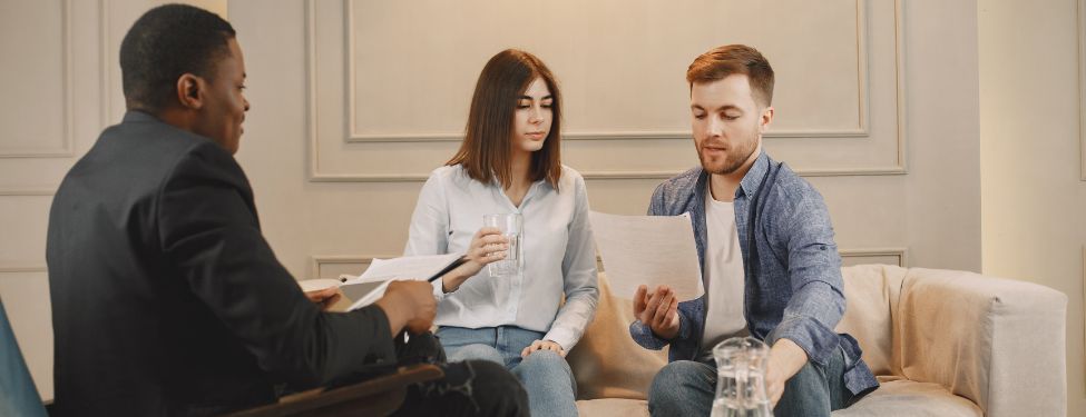 A social work therapist sits across from two clients in a group therapy session.